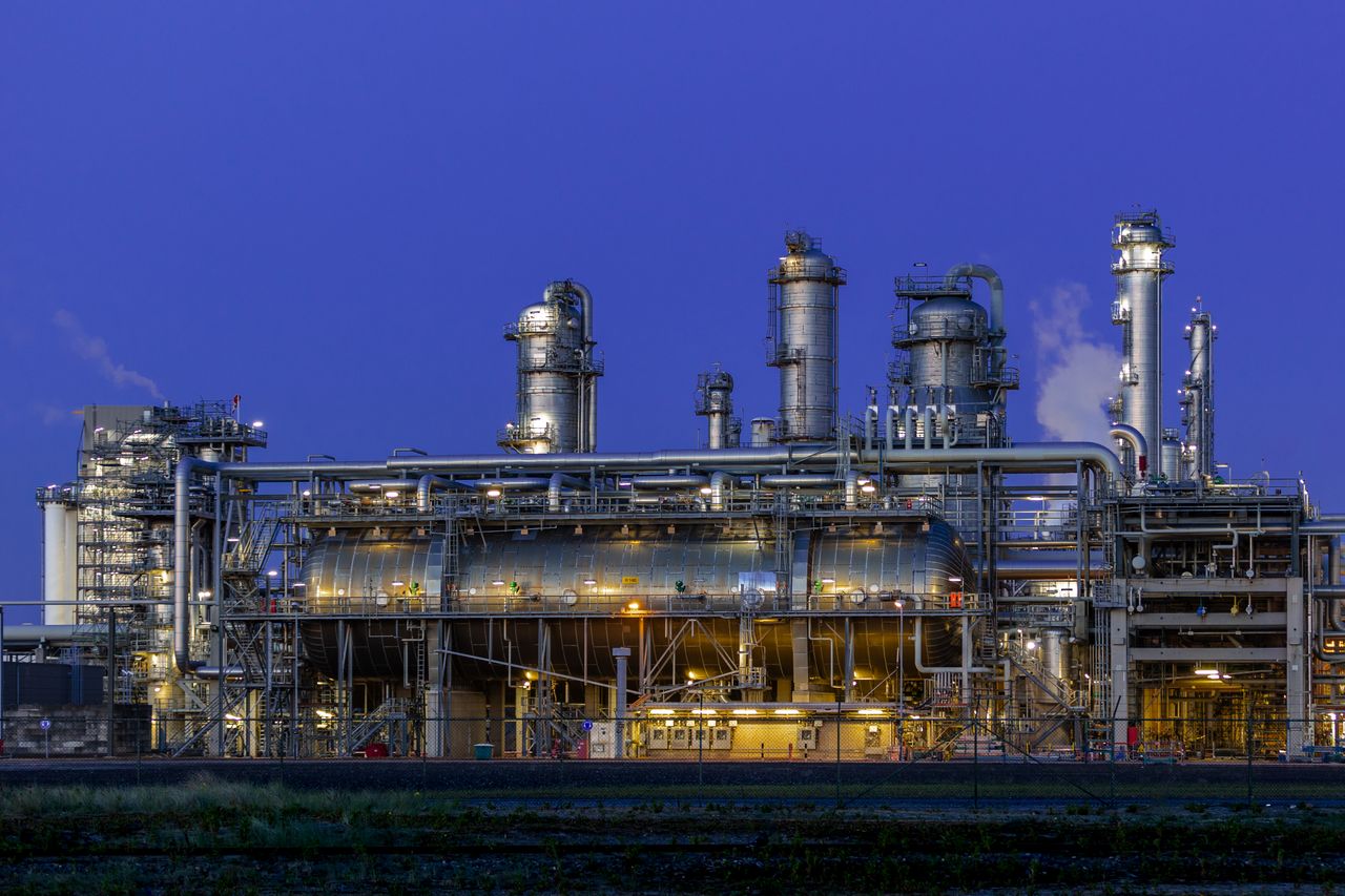 Mastering the First Impression: Your intriguing post title goes here A striking view of an industrial facility in Zuid-Holland, illuminated at dusk against a clear blue sky.